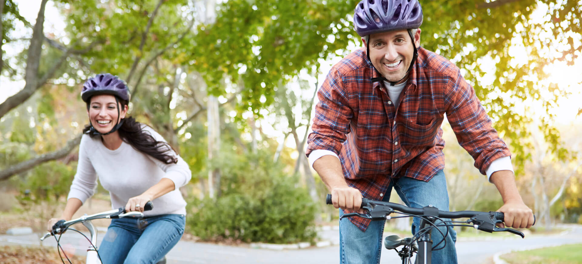 A man and a woman in autumn-weight clothing bike through a park